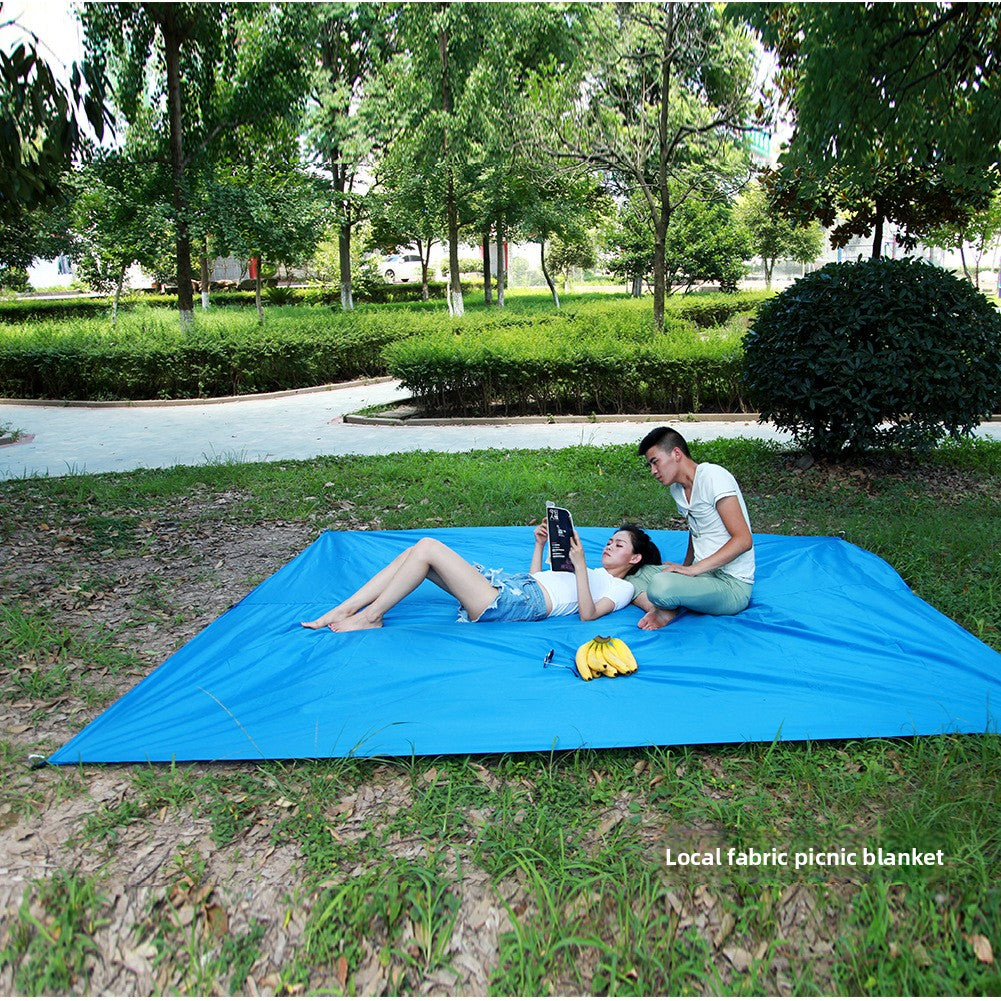 Blue tarp spread flat on grass as a picnic blanket, with two people sitting on it