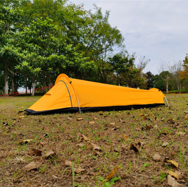 Yellow bivvy tent pitched side-on in open parkland