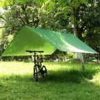 Green tarp pitched as a lean-to in woodland, sheltering a folding bike