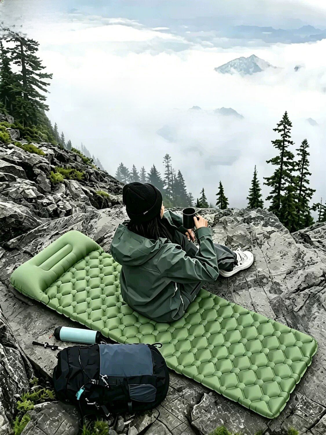 A camper sitting on the inflatable mat on a rocky outcrop above the clouds