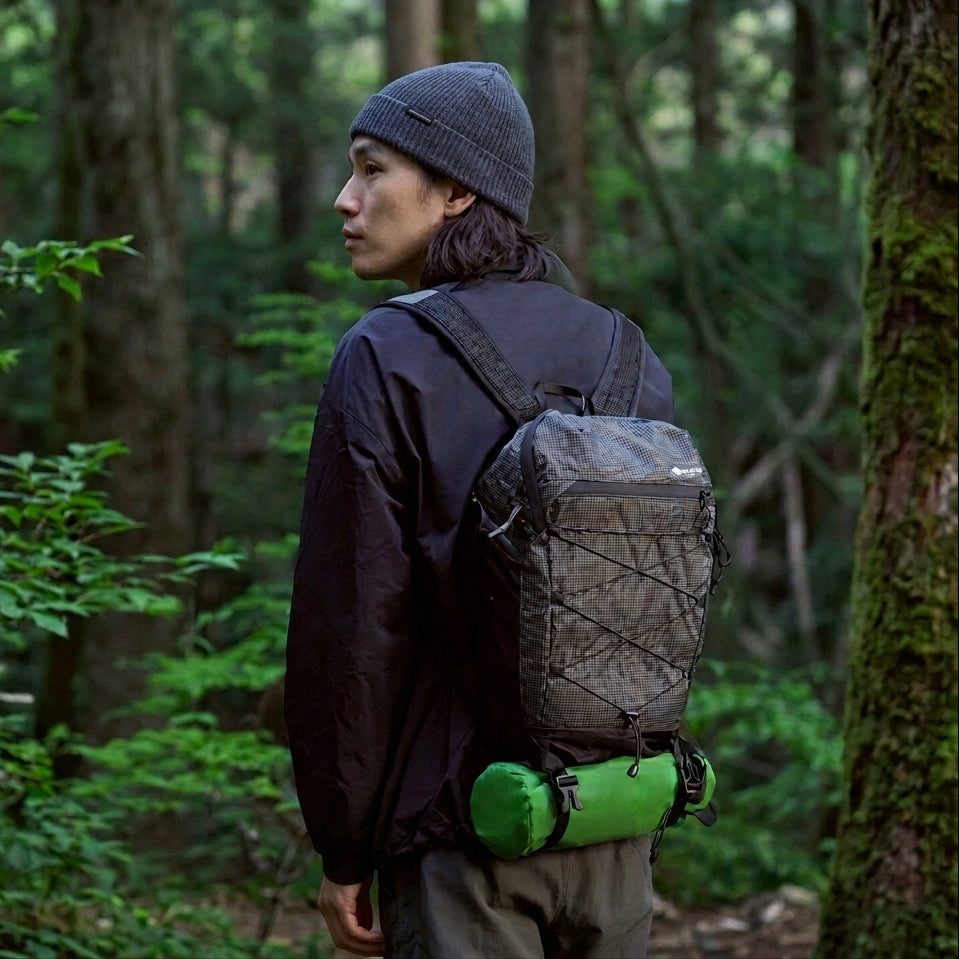 A hiker in woodland with the packed sleeping mat in its stuff sack strapped under a daypack.