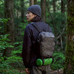 A hiker in woodland with the packed sleeping mat in its stuff sack strapped under a daypack.