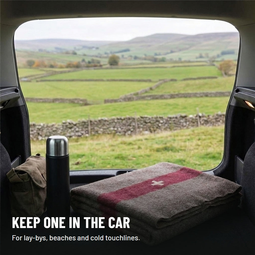 Folded blanket in a car boot next to a flask, with fields and stone walls outside